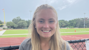 The smiling face pictured here is that of Coach Kelly, standing in front of the football field.