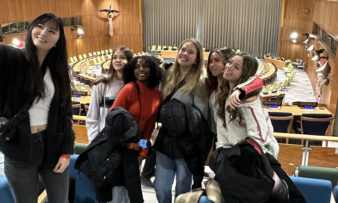 A group of delegates smile for a picture inside the UN assembly room 
